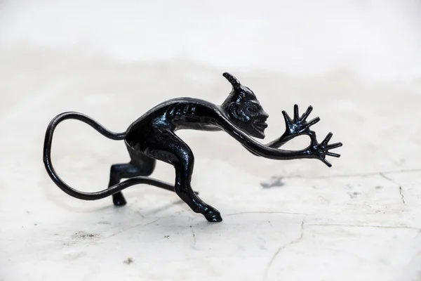 A small metal sculpture of the devil with a tail showing his tongue