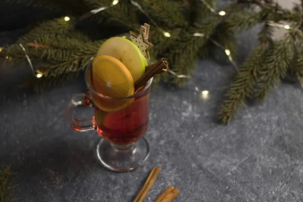 A glass of hot mulled wine, spices, cinnamon, and christmas tree on a black background — Stock Photo, Image