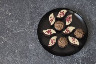 Siyah arka planda siyah bir tabakta farklı türde çikolatalar.