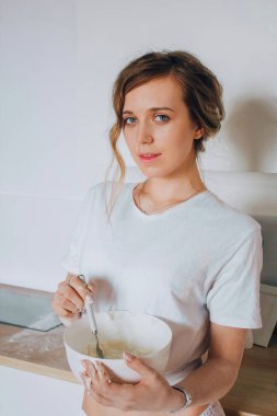 Beyaz bir mutfaktaki kız hamuru, mükemmel vücudu ve sarı saçı hazırlıyor.