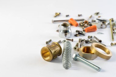 Beyaz zemin üzerinde metal nesneler. İnşaat ve ev tamiratı için detaylar. Masada yatan bir grup nesne. Yedek parça ve parçalar bir yığın halinde duruyor. Sürgüler. fındık, vida, bahar.