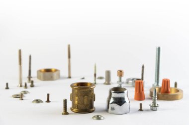 Beyaz zemin üzerinde metal nesneler. İnşaat ve ev tamiratı için detaylar. Masada yatan bir grup nesne. Yedek parça ve parçalar bir yığın halinde duruyor. Sürgüler. fındık ve vida.