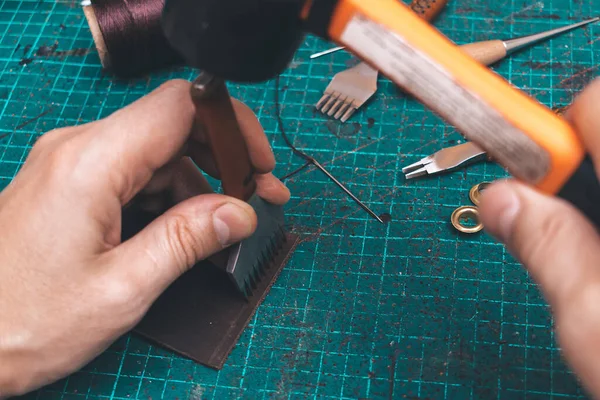 Men's hands make a leather product.Punching holes in the leather with a punch.Tools for leather craft.Top view