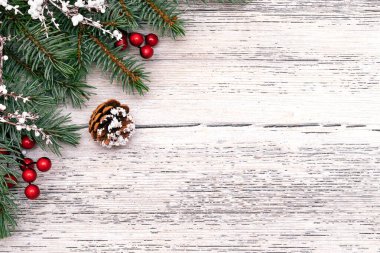 Beyaz ahşap arka planda köknar ağacı dalları, beyaz dallar, kırmızı böğürtlenler ve konilerden yapılmış Noel çerçevesi. Noel arkaplanı. Yazı, üst görünüm, düz yatış alanı kopyala