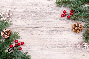 Beyaz ahşap arka planda köknar ağacı dalları, beyaz dallar, kırmızı böğürtlenler ve konilerden yapılmış Noel çerçevesi. Noel arkaplanı. Yazı, üst görünüm, düz yatış alanı kopyala