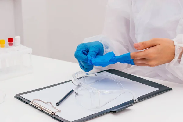 Doctor in a protective suit in the medical office takes off his latex gloves.Safety glasses and writing paper on the table.Coronavirus concept.