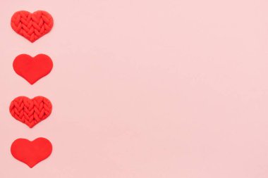 Pembe arka planda plastikten yapılmış kırmızı dokulu kalpler. Sevgililer Günü arka planı. Düz yatış, kopyalama alanı, üst görünüm..