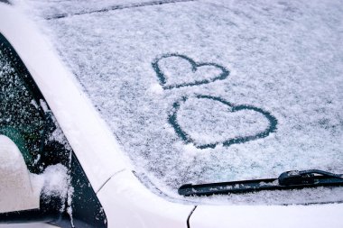 Karla kaplı bir arabanın ön camında parmakları çizilmiş kalpler. Sevgililer Günü kavramı. Metin için boşluk kopyala.