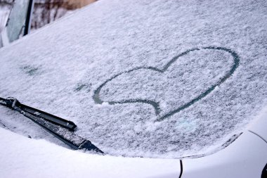 Karla kaplı bir arabanın ön camında parmak izi olan kalp. Sevgililer Günü kavramı. Yaratıcı Sevgililer Günü geçmişi. Metin için alanı kopyala.