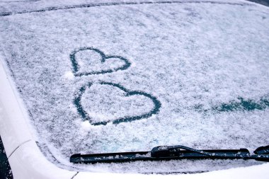 Karla kaplı bir arabanın ön camında parmakları çizilmiş kalpler. Sevgililer Günü kavramı. Metin için boşluk kopyala.
