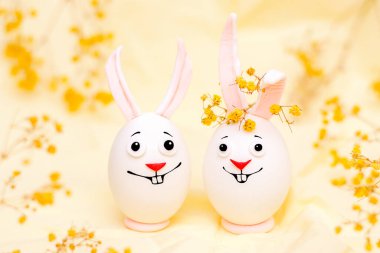 Mutlu Paskalya kavramları. Üzerinde komik yüzler olan yumurtalardan yapılmış yaratıcı Paskalya tavşanları. Sarı arka plan, taze çiçekler..