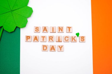 Yeşil kağıdın origami tekniğinde katlanmış bir yonca yaprağı. İrlanda bayrağı renginde bir arkaplanda. Aziz Patrick Günü kavramı. Üst manzara, düz uzanma.