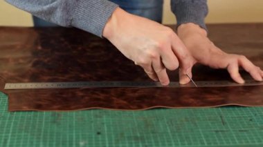 Tanner cetvel ve tente ile kahverengi deri bir yaprak üzerinde işaretler yapıyor. El yapımı deri üretimi. Hobi kavramı..