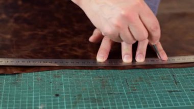 Tanner cetvel ve tente ile kahverengi deri bir yaprak üzerinde işaretler yapıyor. El yapımı deri üretimi. Hobi kavramı..