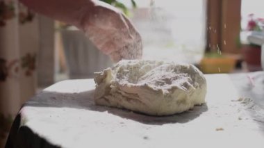 Bir kadın hamuru yoğurur ve mutfak masasına un serper. Eller yukarı, yavaş çekim..
