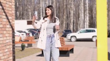Mutlu bir esmer kız, şehir caddesinde yürürken kendini akıllı bir telefonla videoya çeker..