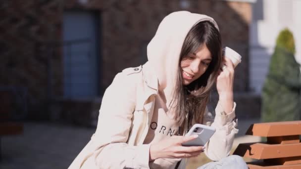 Menina Morena Positiva Usando Smartphone Bebendo Café Uma Rua Bench — Vídeo de Stock