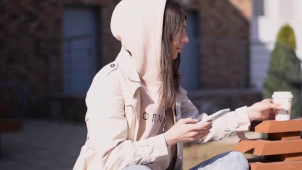 Menina Morena Positiva Usando Smartphone Bebendo Café Uma Rua Bench — Vídeo de Stock
