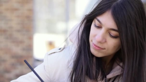 积极的黑发女孩在街上的长椅上的笔记本上做笔记 慢动作 — 图库视频影像