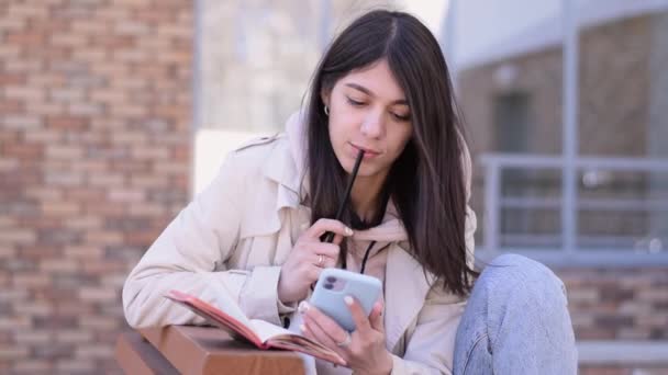 Chica Morena Feliz Usando Teléfono Inteligente Tomando Notas Cuaderno Banco — Vídeos de Stock