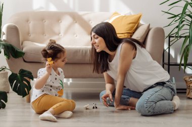 Koyu saçlı, genç, melez bir kadın. Küçük kızıyla yerde oynuyor. Ev dekorasyonu. Birlikte geçirdiğimiz zaman..