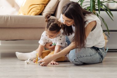 Koyu saçlı, genç, melez bir kadın. Küçük kızıyla yerde oynuyor. Ev dekorasyonu. Birlikte geçirdiğimiz zaman..