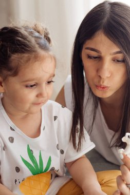 Koyu renk saçlı, genç, melez bir kadın, küçük kızıyla yatakta oynuyor. Ev dekorasyonu. Birlikte geçirdiğimiz zaman..