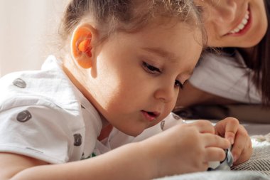 Koyu renk saçlı, genç, melez bir kadın, küçük kızıyla yatakta oynuyor. Ev dekorasyonu. Birlikte zaman geçirme. Aile kavramı ve Anneler Günü kavramı..