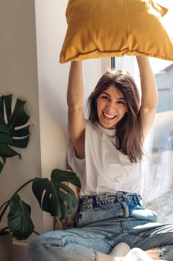 Koyu renk saçlı melez bir kız pencere eşiğinde mutlu bir şekilde oturuyor.