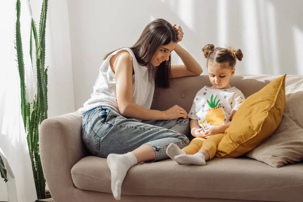 一位黑头发的年轻男女和她的小女儿在沙发上玩耍 家庭室内设计和家庭计划 时间在一起 家庭观念和母亲节观念 — 图库照片