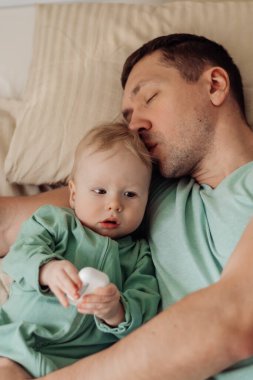 Genç mutlu baba kucağında küçük oğluyla yatakta yatıyor.