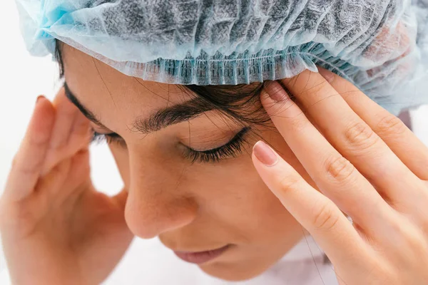 Tired medical worker in a protective clothing closes her eyes and holds her head.Medical and coronavirus concept.