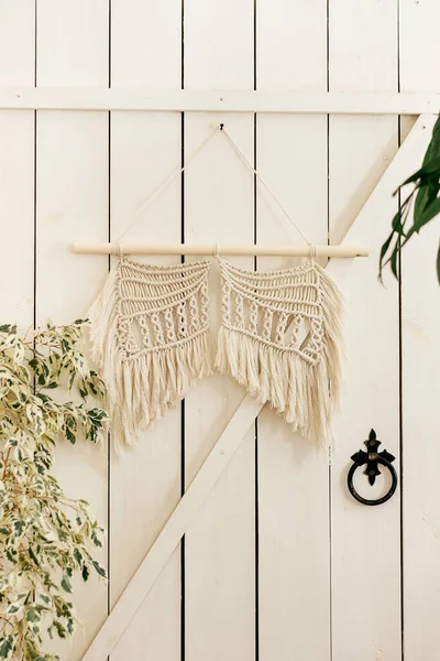 Wall decor woven from white cotton threads in the macrame style hangs on a white wooden wall.Handmade concept.Home decor.