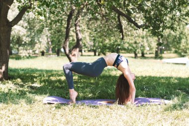 Spor giyiminde yoga, Bridge yaz gününde parkta poz veriyor. Spor ve Yoga eğitimi, sağlıklı yaşam tarzı..