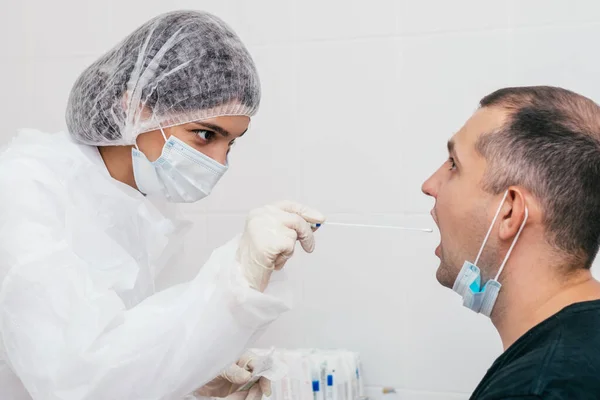 A medical worker taking mouth swab from middle-aged man to test for possible coronavirus infection in clinic.Medical and coronavirus concept.