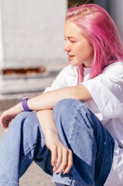 Pozitif pembe saçlı, beyaz tişörtlü ve mavi kotlu genç bir kızın portresi. Sokak tarzı. Z kuşağı tarzı..