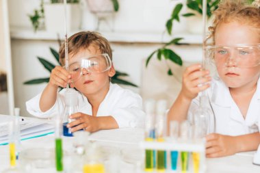 Ciddi küçük bir çocuk ve beyaz üniformalı bir kız, laboratuarda kimyasal deneyler yapıyorlar. Okul konseptine geri dönüyorlar. Genç bilim adamları. Anaokulu ve çocukların okul öncesi eğitimi..