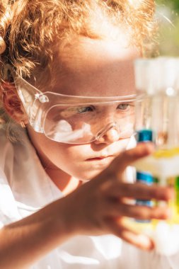 Laboratuvarda kimyasal deneyler yapan beyaz üniformalı küçük kızıl saçlı bir kızın fotoğrafını çek. Okul konseptine geri dön. Genç bilim adamları. Anaokulu ve çocukların okul eğitimi..