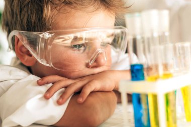 Beyaz üniformalı ciddi bir çocuk laboratuarda kimyasal deneyler yapıyor. Okula geri dönüyor. Genç bilim adamları. Anaokulu ve çocukların okul öncesi eğitimi..