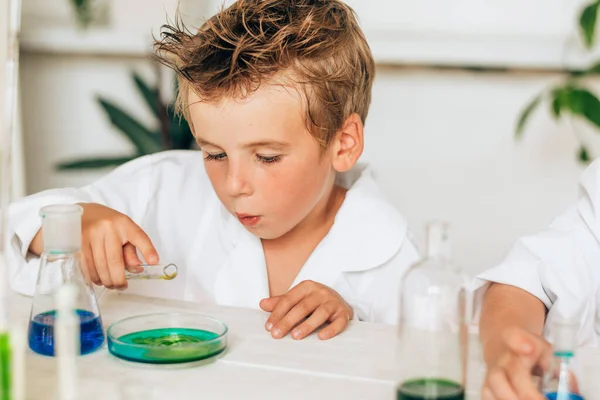 Curious little boy in white uniform conducts chemical experiments in a laboratory.Back to school concept.Young scientists.Natural sciences.Preschool and school education of children.