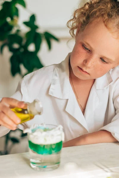 Little red-haired girl in white uniform conducting chemical experiments in a laboratory.Back to school concept.Young scientists.Natural sciences.Preschool and school education of children.