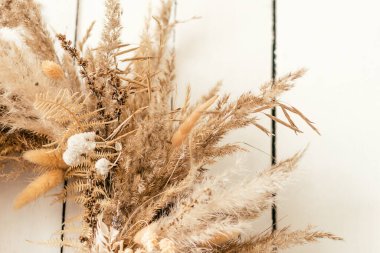 Kurumuş bitkilerden, çiçeklerden ve dikenlerden oluşan güzel bir çelengi beyaz ahşap bir duvara asar..