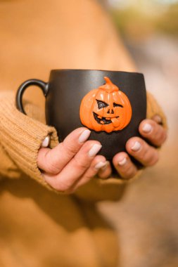 Siyah kupa ve sıcak çay kadının ellerinde. Kupa balkabağı Jack O 'Lantern ile süslenmiş. Cadılar Bayramı konsepti..
