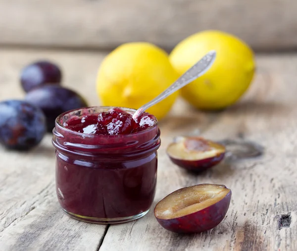 Plum jam in glazen pot en citroen op rustieke houten bord — Stockfoto