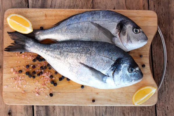 Two fresh gilt-head bream fish on cutting board — Stock Photo, Image