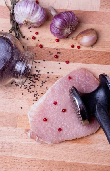 Raw pork schnitzel with meat tenderizer on wooden board — Stock Photo, Image