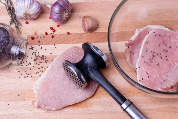 Raw pork schnitzel with meat tenderizer on wooden board — Stock Photo, Image