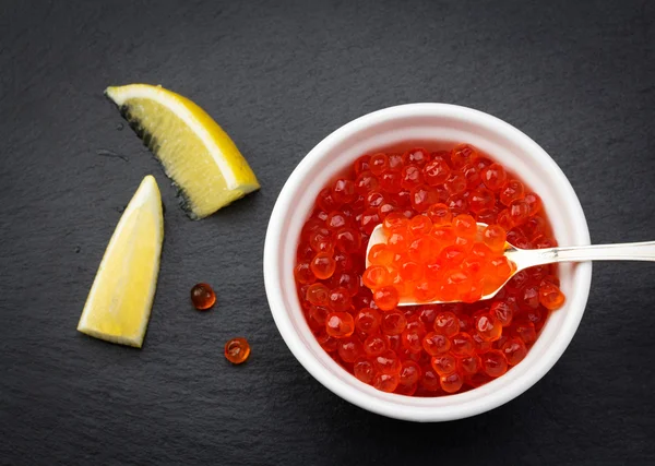 Lemon and white bowl with salmon caviar standing on black slate plate — Stock Photo, Image