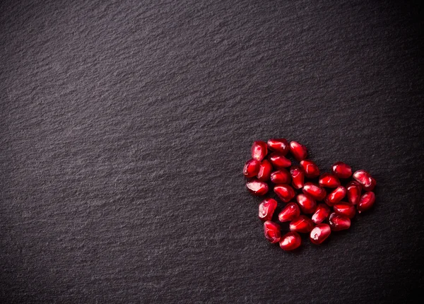 Olgun nar taneleri siyah arduvaz arka plan üzerinde kalp şeklinde