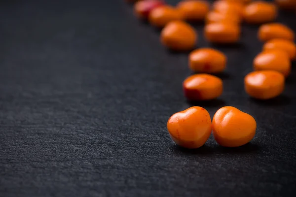 Orange heart shaped pills or candy on grunge black slate background. Copy space. — Stock Photo, Image